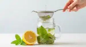 A hand straining a homemade lemon balm recipe for weight loss into a mason jar mug.