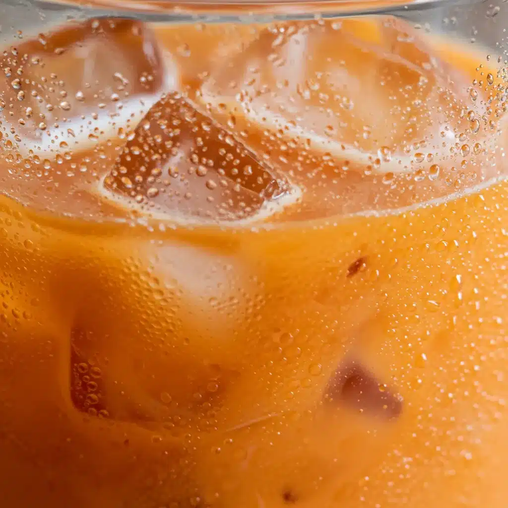 Thai Tea Recipe (Authentic & Easy) 5 A macro photograph of a glass of iced Thai tea, showing condensation droplets on the cold glass and ice cubes submerged in the orange drink.