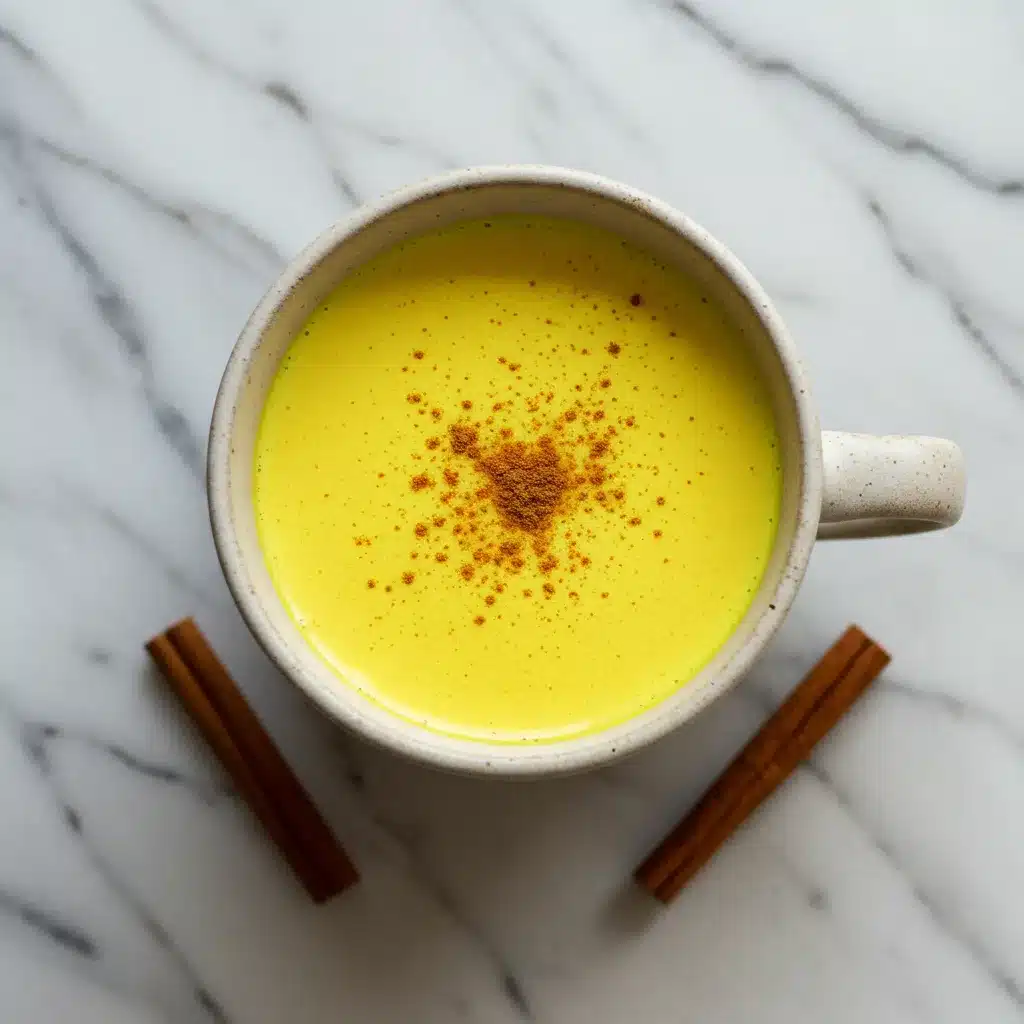 The Ultimate Turmeric Milk Recipe (Easy Golden Milk) 5 Overhead shot of a mug of golden turmeric milk, garnished with cinnamon, with two cinnamon sticks placed on a marble surface.