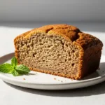 A thick slice of moist banana bread with almond flour on a white plate, showing its tender texture.