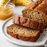 A sliced loaf of moist banana bread with applesauce on a white plate.