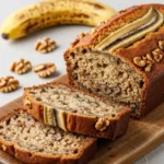 A loaf of moist banana nut bread sliced on a wooden board to show the fluffy interior with walnuts.