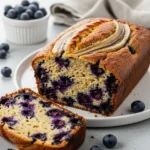A loaf of moist blueberry banana bread with a slice cut out, showing a tender crumb filled with berries.