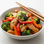 A close up 45-degree angle shot of a bowl of chicken stir fry recipe with broccoli, carrots, and bell peppers.