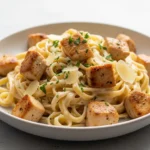 A close-up 45-degree angle shot of a bowl of creamy chicken alfredo recipe, garnished with fresh parsley.