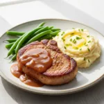 A tender crockpot pork chop on a plate, smothered in rich brown gravy and served with mashed potatoes.