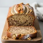 A loaf of moist eggless banana bread sliced on a wooden board to show its tender texture.