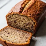 A moist slice of gluten free banana bread leaning against the full loaf, showing the tender texture.