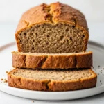 A close up 45-degree angle shot of a freshly baked healthy banana bread loaf, with one slice cut to show its moist and tender crumb.