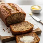 A sliced loaf of moist keto banana bread on a wooden board, with two slices in front.