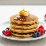 A stack of fluffy keto pancakes with melting butter and sugar-free syrup being poured on top.