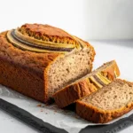 Sourdough Banana Bread Recipe (Use Your Sourdough Discard!) A loaf of sourdough banana bread recipe, partially sliced to show the moist crumb inside.