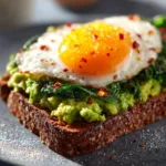 A close-up shot showing the creamy texture of mashed avocado on a perfectly toasted slice of sourdough bread, ready to be spread.