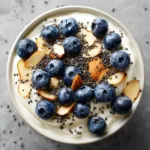 A close-up macro shot of the creamy texture of a high protein Greek yogurt base in a white bowl before toppings are added.