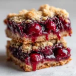 An extreme close-up of two thick cherry pie bars, showing the crumbly shortbread crust texture and the gooey cherry pie filling.