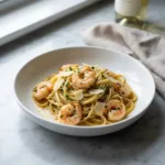 A close-up, elevated shot of a bowl of garlic butter shrimp pasta, garnished with fresh parsley.