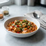 A close-up, slightly elevated shot of a bowl of healthy chicken tikka masala, garnished with fresh cilantro, sitting on a marble surface.
