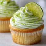 An extreme close-up of a key lime cupcake, showing the moist cake crumb, a layer of graham cracker crust, and a perfect swirl of cream cheese frosting with lime zest.