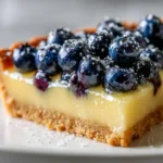 Lemon Blueberry Tart Recipe A close-up slice of lemon blueberry tart on a white plate, showcasing the silky lemon curd filling and buttery shortbread crust.