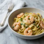 A close-up, slightly elevated view of a white bowl filled with lemon garlic butter shrimp pasta, garnished with fresh parsley.