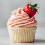 A close-up shot of a single strawberry lemonade cupcake, showcasing the fluffy texture of the lemon cake and the creamy swirl of the pink strawberry buttercream frosting.