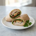 Whole Wheat Turkey Hummus Wrap: Your 10-Minute Healthy Lunch A healthy whole wheat turkey hummus wrap sliced in half on a white plate.