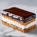 A 9x13 inch pan of layered eclair dessert before the chocolate topping is added, showing the creamy vanilla filling and graham crackers.