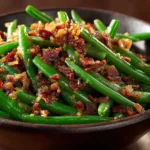 An extreme close-up, top-down view of vibrant green beans mixed with crispy bacon pieces and a rich, dark glaze.
