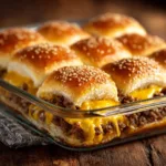 Cheeseburger Sliders: The Ultimate Party Food A batch of baked cheeseburger sliders in a baking dish, with melted cheddar cheese peeking out from under the golden-brown Hawaiian rolls.