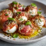 A close-up view of golden-brown baked prosciutto wrapped mozzarella balls, showing the crispy texture of the prosciutto and the softly melted cheese inside.
