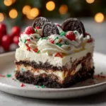 A perfect square slice of Christmas Oreo dessert lasagna on a white plate, showing the distinct layers of Oreo crust, cream cheese, and chocolate pudding.