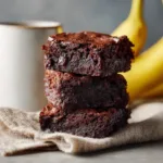 3 Ingredient Banana Brownies: The Easiest Fudgy Treat Ever A close-up shot of three fudgy dark chocolate banana brownies arranged neatly, highlighting their moist and dense crumb.