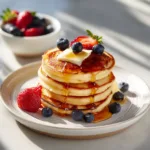 A close-up shot of fluffy gluten-free pancakes made with coconut flour, garnished with fresh berries and a pat of butter.