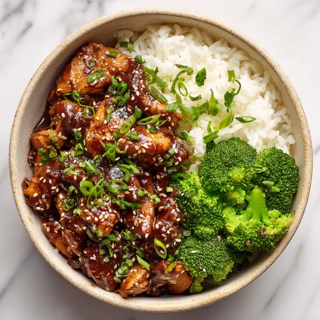 A fresh teriyaki chicken bowl being assembled with rice, perfectly cooked chicken, steamed broccoli, and shredded carrots.