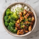 A close-up overhead shot of a teriyaki chicken rice bowl with fresh broccoli and carrots, showcasing the glossy homemade teriyaki sauce.