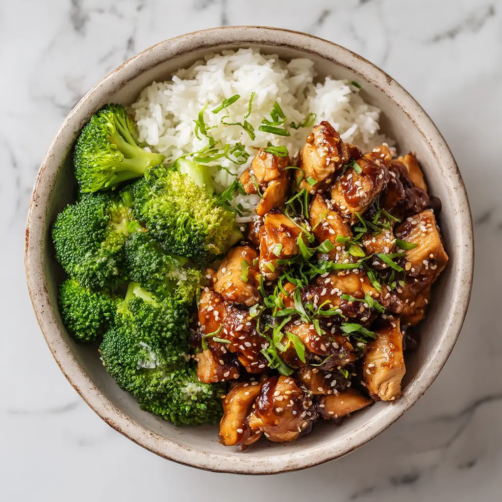 A close-up overhead shot of a teriyaki chicken rice bowl with fresh broccoli and carrots, showcasing the glossy homemade teriyaki sauce.