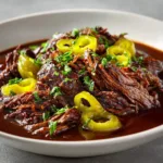 A 4-pound chuck roast in a slow cooker, topped with a stick of butter, ranch seasoning, au jus mix, and pepperoncini peppers before cooking.
