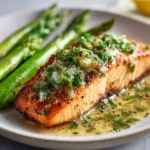 A perfectly pan-seared salmon fillet with crispy skin, resting on a plate before being added to the creamy sun-dried tomato sauce.