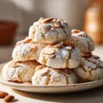 A pile of soft Italian almond ricotta cookies on a wooden board, showcasing their light and crinkly texture before being glazed.