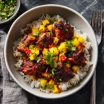 A plate of sticky Asian glazed chicken served over a bed of white rice, ready to eat. The chicken is glistening with the honey-soy sauce.