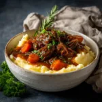 A close-up overhead shot of a rustic white bowl containing apple cider beef stew. Chunks of beef, carrots, and potatoes are visible in the savory broth.