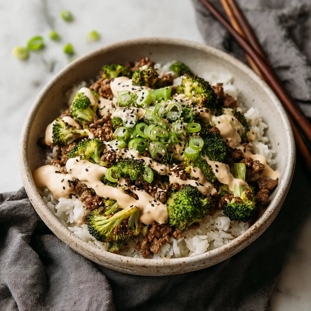 A close-up eye-level shot of a bowl of ground beef and broccoli stir fry served over white rice.