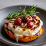 A thick, roasted orange sweet potato round with caramelized, slightly charred edges topped with melted gooey white brie cheese for Holiday Appetizers.