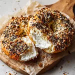 Close-up of a golden brown, blistered bagel crust generously coated in sesame, poppy seeds, minced garlic, and coarse sea salt. (New York Style Bagels Recipe)