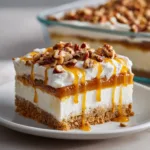 A perfect slice of Pecan Pie Lasagna on a white plate, showing its distinct layers of graham cracker crust, cheesecake filling, caramel pecan sauce, and whipped cream. (Pecan Pie Lasagna)