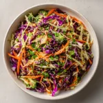 Top-down view of fresh purple and pale green cabbage, julienned carrots, and broccoli for an Asian Cabbage Salad.