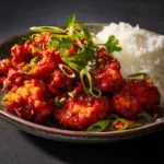 A close-up shot of crispy Dragon Chicken, showing the glossy texture of the spicy Indo-Chinese sauce and garnished with spring onions.