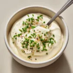 A close-up shot of creamy Horseradish Sauce for Prime Rib blended with Dijon mustard flecks and garnished with chopped fresh chives.