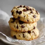 The Ultimate Soft-Baked Cottage Cheese Protein Cookies A close-up of golden-brown cottage cheese protein cookies speckled with dark semi-sweet chocolate chips on a matte white ceramic plate.