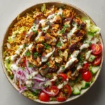 Close-up overhead shot of a Chicken Shawarma Crispy Rice Salad in a ceramic bowl showcasing heavily charred spiced chicken and chopped fresh vegetables.